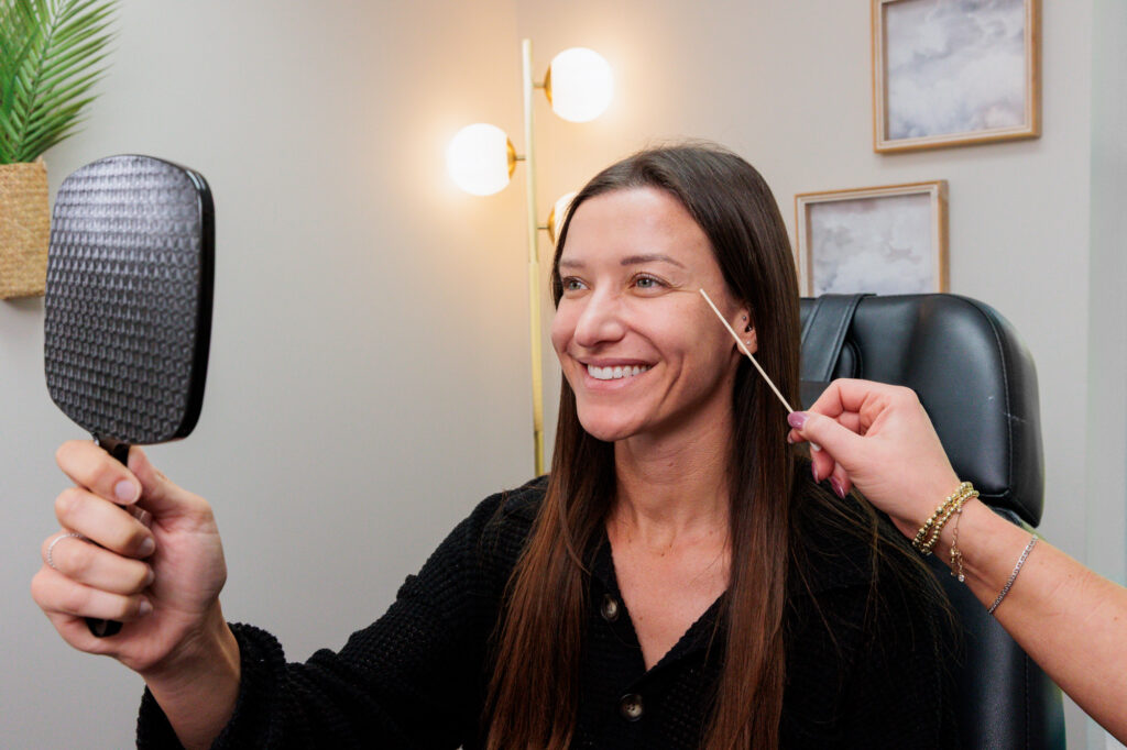 A patient consults with Dr. West and uses a mirror to discuss her skin goals before scheduling laser skin resurfacing in Ann Arbor.